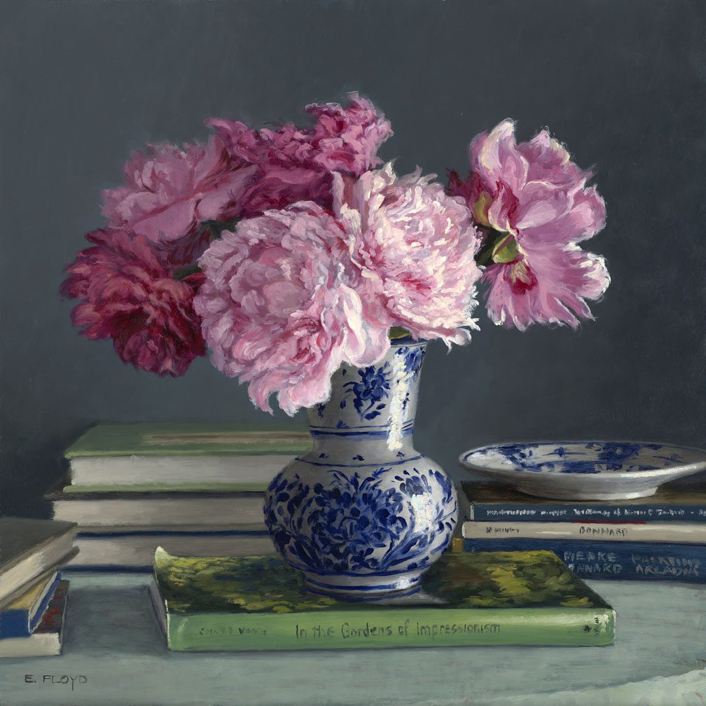 A blue and white vase holding pink flowers on a table with books.