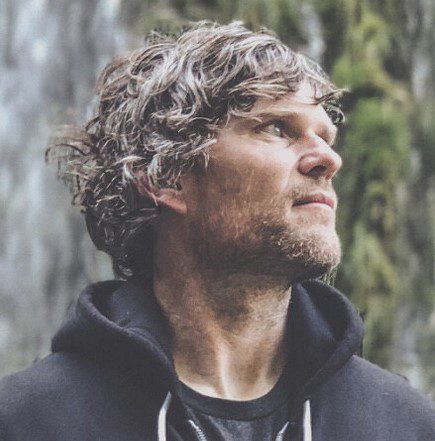 Profile of a man with curly hair looking contemplative outdoors.