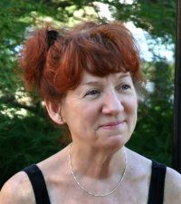 Smiling woman with red hair outdoors in a natural setting.