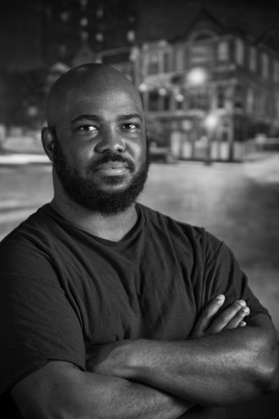 Confident man with arms crossed in a nighttime urban setting.