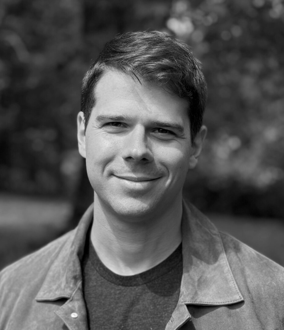 Black and white portrait of a smiling man outdoors.