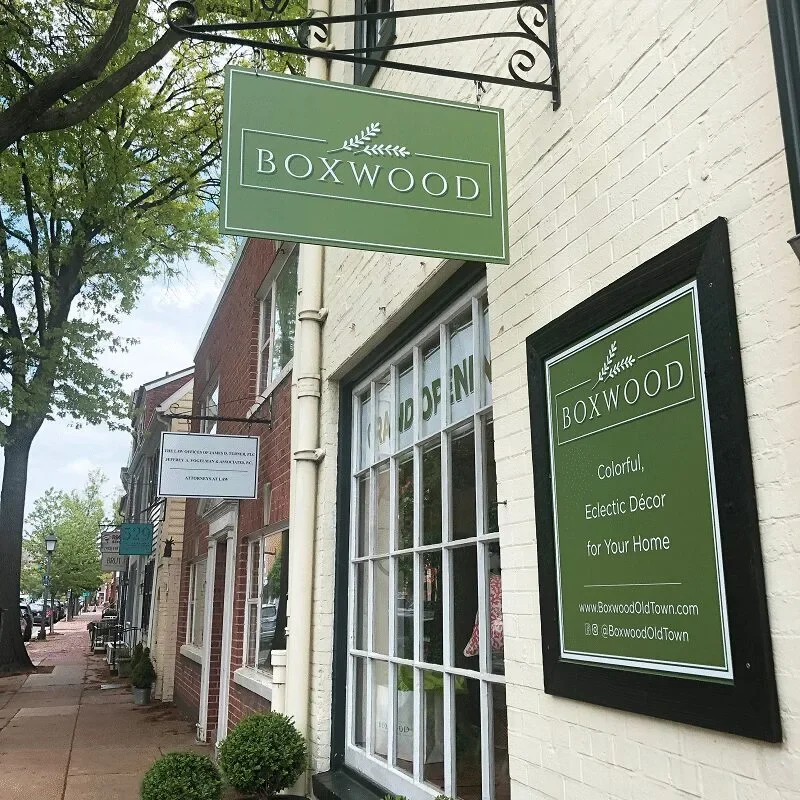Signage for Bowood boutique on a quaint street with trees.