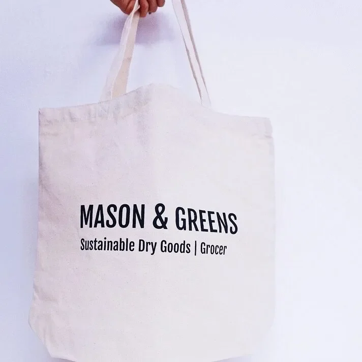 A white tote bag with Mason & Greens branding and sustainable goods message.